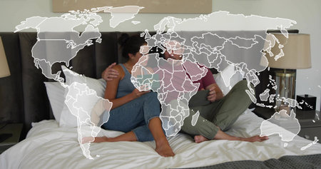 Sitting couple in bedroom, wearing casual clothes, holding phone on king bed with world map overlay. Romance, intimacy, partners, cozy, interior, neutral, lifestyleの写真素材