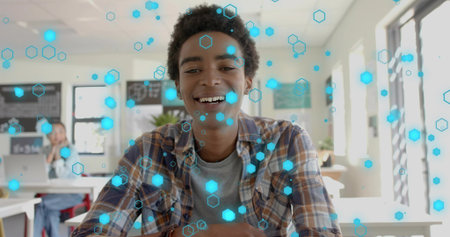 Smiling male student wearing plaid shirt leaning on desk in classroom, showing blue hex overlay. Learners, edtech, laptop, education, learning, collaboration, modernの写真素材