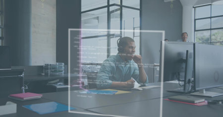 Reviewing developer wearing headset and light shirt debugging code on large monitor in open office. Collaboration, teamwork, modern, glass, partitions, productivity, greeneryの写真素材
