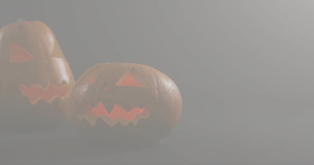 Glowing carved pumpkins emitting warm orange light in dim foggy studio on matte surface, copy space. Lanterns, gourds, candlelight, hazy, moody, reflections, grayの写真素材