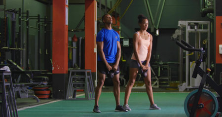 Holding weights, two partners wearing blue tee and pink tank performing deadlift, with bike. Duo, gymgoers, industrial, strength, teamwork, functional, focusの写真素材