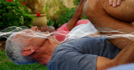Lying senior in gray shirt stretching in garden with potted red flowers, dotted white wave graphic. Elder, outdoor, wellness, gentle, exercise, backyard, lawnの写真素材