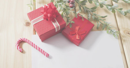 Displaying two red gift boxes with ribbons on light wooden table, candy cane and foliage. Presents, seasonal, flatlay, stock, home, warmth, decorの写真素材