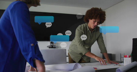 Leaning man in olive shirt pointing to plans in meeting room, woman in blue blazer observing. Blueprints, collaboration, architect, designer, planning, conference, boardroomの写真素材