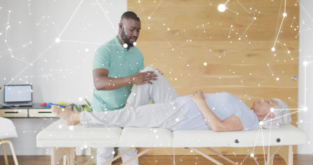 Bending therapist supporting senior patient right knee on therapy table, in green polo, laptop left. Rehabilitation, physiotherapist, elderly, leg, assessment, supine, clinicの写真素材