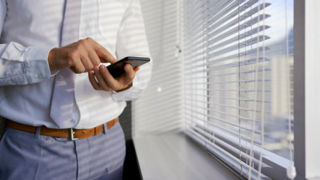Adult businessman is tapping smartphone by blinds wearing shirt, tie in flat design business scene....