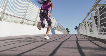 Sprinting female runner powering up curved footbridge, in purple tank, floral leggings, white shoes....