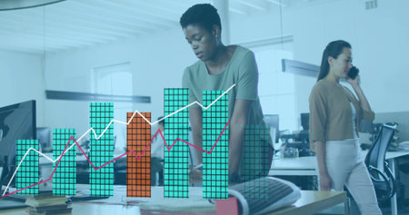 Leaning central woman wearing green top dark pants examining documents in open office chart overlay. Collaboration, teamwork, data, analytics, workflow, workspace, focusの写真素材