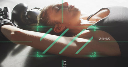 Lying female athlete resting on padded mat at gym, black top, gloves, green HUD numeric readouts....