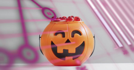 Sitting orange jack-o'-lantern bucket holding red gummies on white tabletop, pink reflections. Pumpkin, lantern, plastic, candies, diffused, softlight, studioの写真素材