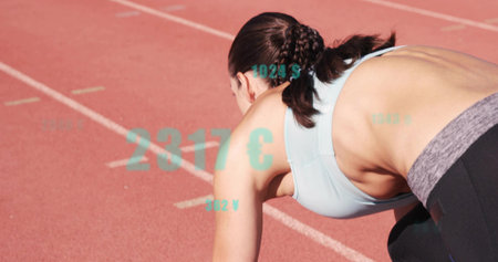 Crouching female runner preparing to sprint on red track with lanes, in sportswear, teal graphics. Athlete, training, outdoors, focus, motion, speed, competitionの写真素材
