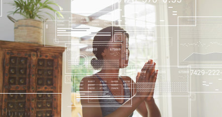 Praying woman wearing gray tank at home near window, with over-ear headphones and UI overlays....