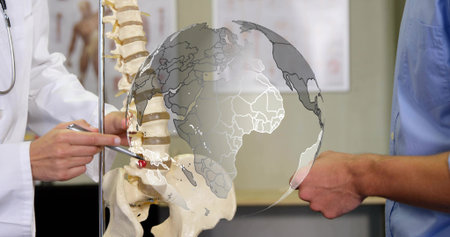 Pointing doctor in lab coat with stethoscope indicating vertebra on spine model in clinic, globe. Anatomy, education, demonstration, skeleton, classroom, medical, instructionの写真素材