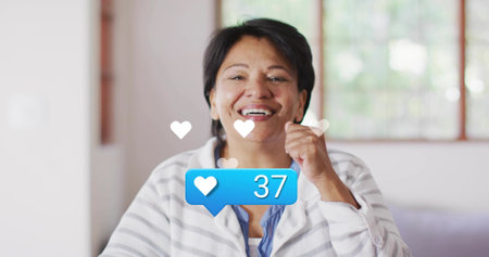 Smiling senior Indian woman raising fist by chin at home, showing blue bubble 37, wearing cardigan....