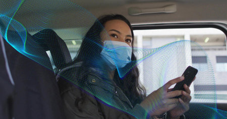 Holding phone, woman in surgical mask, dark jacket in rear-seat looking at window with wave overlay....