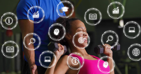 Pressing woman in pink top lifting dumbbells at gym bench, blue-shirt trainer spotting. Fitness, weights, training, athletic, focus, determination, dynamicの写真素材