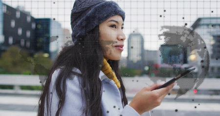 Holding smartphone, woman wearing yellow scarf gazing ahead on bridge, earbud. Urban, commuter, map, cityscape, walkway, overcast, calmの写真素材