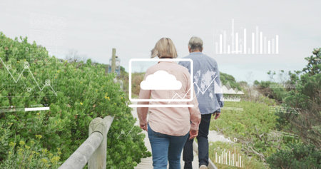 Walking senior pair in pale and blue shirts along wooden boardwalk with handrail. Coast, trail,...