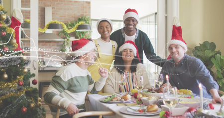 Gathering six people wearing Santa hats sitting around dining table at home, with Christmas tree. Guests, holiday, candles, garland, stockings, kitchen, daylightの写真素材