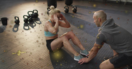 Crunching female trainee in athletic wear while trainer holding feet at gym, with kettlebells. Fitness, workout, training, weights, coach, facility, functionalの写真素材