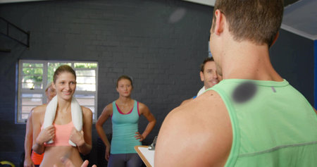Leading instructor in green tanktop holding clipboard in gym, with towel and kettlebell, copy space....