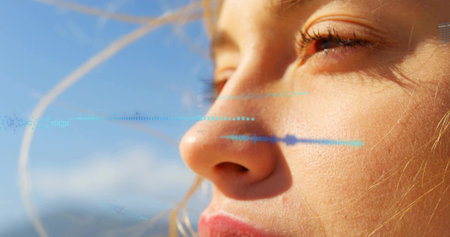 Soaking woman's face in warm sunlight at coastal horizon, with blue waveform overlay and hair. Portrait, closeup, outdoors, sky, clouds, digital, stripeの写真素材