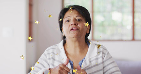 Gesturing senior woman in striped sweater speaking in living room, with gold star overlays....