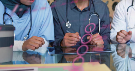 Reviewing medical team in scrubs white coat at clinic leaning over tablet with stethoscopes, notes. Nurse, physician, colleagues, teamwork, healthcare, glass, tableの写真素材