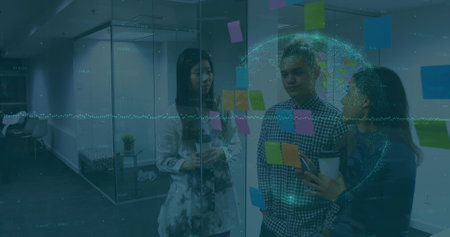 Discussing colleagues pointing at colorful post-its on glass partition in office, with hologram....