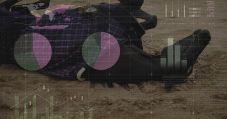 Lying male wearing purple shirt, belt and black boots on sand, showing pie charts and graphs. Prone,...