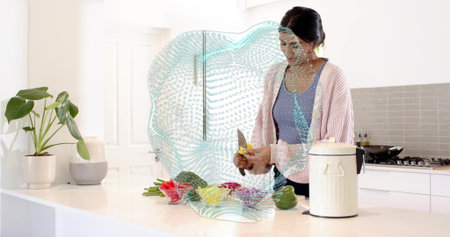 Chopping mid-adult Indian woman in blue tank and cardigan at home kitchen, with knife, vegetables....
