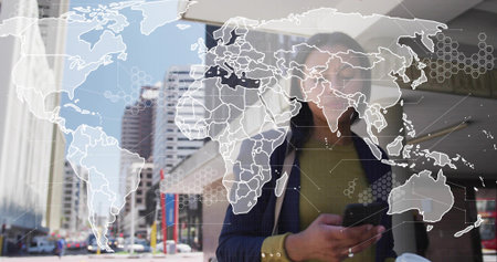 Walking mid adult woman navy blazer green top checking phone holding coffee on street with map....