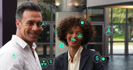 Standing two execs presenting energy visuals in atrium, with floating green icons and formal wear....