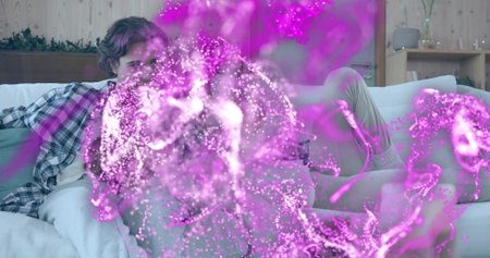 Sitting two women wearing plaid shirt and loungewear on sofa at home, with magenta particle overlay....