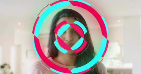 Standing Indian woman wearing pale pink sweater in bright kitchen, with cyan magenta rings overlay....