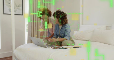 Collaborating two mid-adult women using laptop and notebook in bedroom, denim shirt, green overlay....