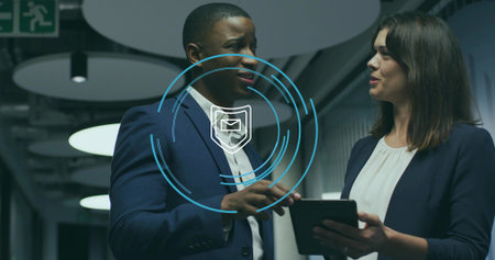 Discussing team members in suits holding tablet in corridor showing email shield icon and exit sign....