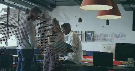 Leaning trio over laptop and papers in modern office, wearing patterned shirt and striped dress....