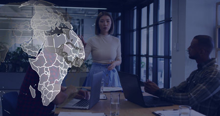 Leading woman in light top, blue skirt guiding meeting at office table, map overlay, laptops....