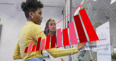 Interacting duo wearing yellow and maroon reviewing 3D bar chart on glass partition in office....