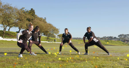 Stretching four women in black-and-white kits doing side lunges on sports field with yellow cones....