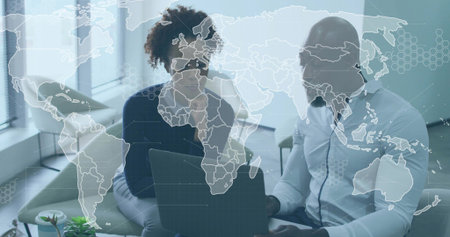 Collaborating pair reviewing laptop in office lounge, with world map overlay, wearing biz-casual....