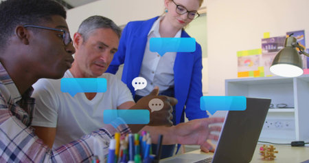 Working three-person team reviewing laptop with chat bubbles at office desk, woman in blue blazer....