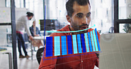 Reviewing man in red shirt analyzing laptop data with translucent chart overlay in open-plan office....