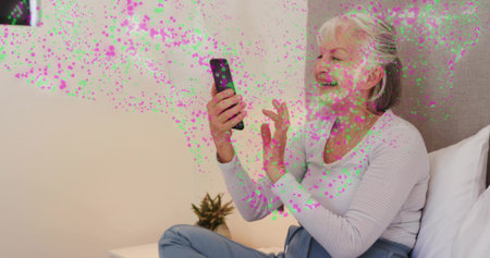 Smiling woman using smartphone in ribbed top on bed with bedside plant and confetti, copy space....