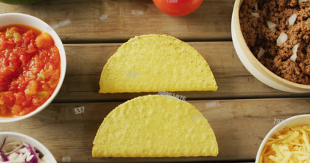 Displaying two yellow hard corn taco shells on rustic tabletop, with salsa, beef, cheese, cabbage....