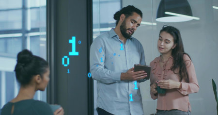 Reviewing team standing in office near glass wall, using tablet and holding mug with binary code....