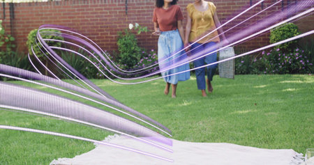 Walking barefoot women in yard to light blanket rust and mustard tops with woven basket purple overlay. Outdoor, picnic, friends, garden, lawn, casual, joyの写真素材