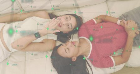 Lying two women talking on sofa cushions, wearing smartwatches, crop top, red tee. Friends,...