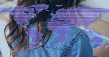 Reading woman in denim jacket at desk viewing blurred right page, with purple world map overlay. Back, silhouette, adult, female, hologram, glitch, augmentedの写真素材